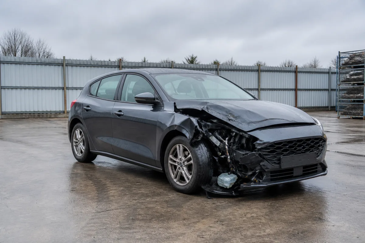 Collision-damaged hatchback awaiting assessment in a salvage yard